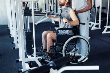 Tekerlekli sandalyede oturan ve spor malzemeleriyle sırtını çalıştıran genç bir hasta ve terapist.