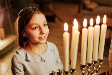 Hanuka kutlamaları sırasında Menorah mumuna bakan gülümseyen Yahudi kızın yüksek açılı portresi.
