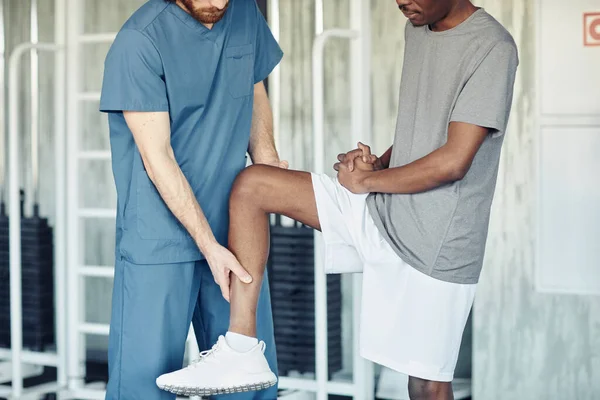 Doctor in uniform examining pain leg of patient in gym before training