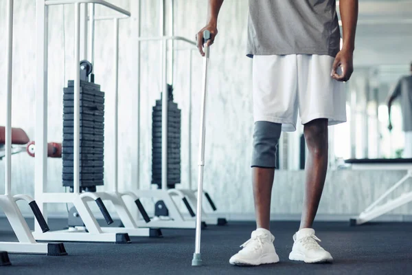 stock image Close-up of African patient walking with walking stick along gym, he holding rehabilitation with his injury leg