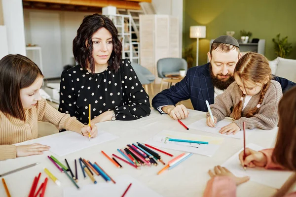 Portrait of modern jewish family drawing together while sitting at table at home with three children