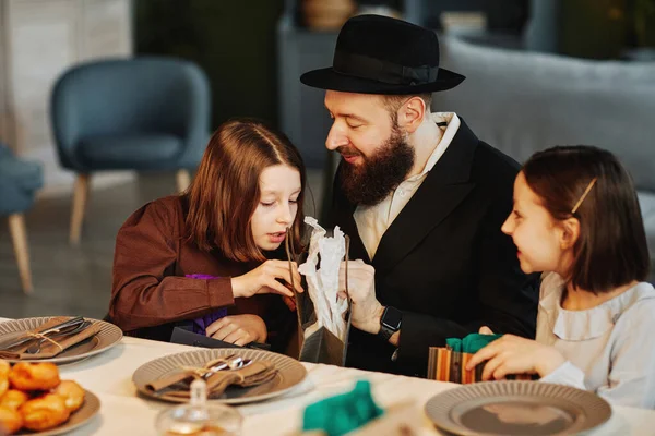 Portrait of modern jewish family sharing presents with children at dinner table in cozy home setting