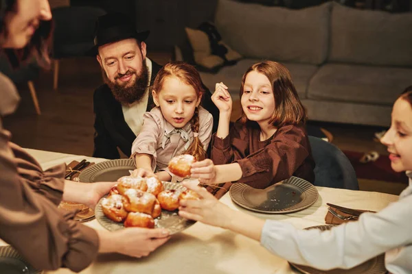 Portrait of orthodox jewish family with children enjoying homemade pastry at dinner table