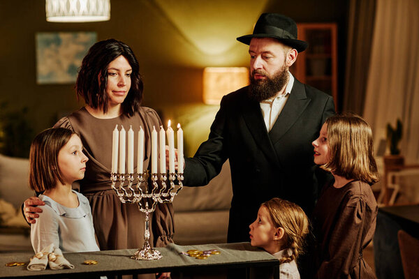 Портрет ортодоксальной еврейской семьи зажигая менору свечи во время празднования Хануки дома