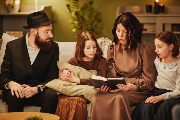 Portrait of traditional jewish family at home with focus on mother reading book