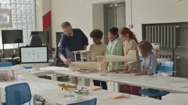 Orta boy beyaz erkek öğretmen el yapımı uçak modelini sınıftaki bir grup çok ırklı ilkokul öğrencisine birlikte mühendislik kulübüne giderken gösteriyor.