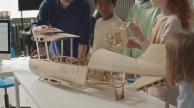 Kafkas erkek öğretmenin el yapımı ahşap uçak modelini çok ırklı okul çocuklarına göstermesi ve ilkokuldaki mühendislik kulübünde ders verirken çalışmalarını açıklaması.
