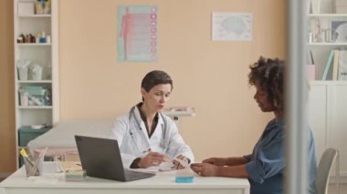 Afrika kökenli Amerikalı bir kadının bebek ultrason taramasına bakarken orta ölçekte beyaz kadın doğum uzmanıyla muayene ve muayene olurken çekilmesi.