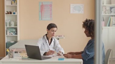 Afrika kökenli Amerikalı bir kadının bebek ultrason taramasına bakarken orta ölçekte beyaz kadın doğum uzmanıyla muayene ve muayene olurken çekilmesi.