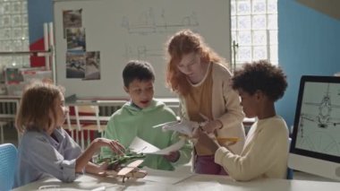 Sınıfta birlikte uçak modelleri yaparken sohbet eden bir grup genç öğrencinin orta boy fotoğrafı.