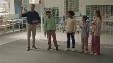 Sınıfta el yapımı ahşap uçaklar fırlatan çok ırklı çocukların ve Kafkas erkek öğretmenlerin tam boy çekimi.