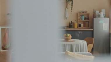 Orta boy hamile bir kadın, örgü bej elbiseli, gündüzleri rahat bir şekilde evde otururken buzdolabında bir şey ararken.