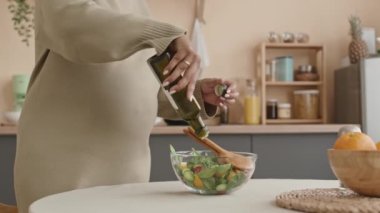 Tanımlanamayan hamile bir kadının, örgü elbise giyip sağlıklı sebze salatasıyla zeytinyağını karıştırdığı ve evde öğle yemeği hazırlarken malzemelerini karıştırdığı sahneler.