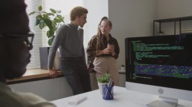 Afrika kökenli Amerikalı meslektaşları masaüstü bilgisayarına yazılım programı kodları yazarken kahve molası sırasında konuşan çok ırklı programcıların orta boy görüntüleri.