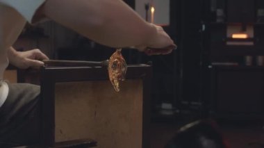 Tanımlanamayan cam üfleyici, cımbız kullanarak atölyedeki sıcak erimiş cam parçasından zarif kıvrımlar oluşturur.