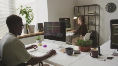 Minimalist açık uzay ofisinde birlikte çalışırken bilgisayarlara programlama kodları yazan çok ırklı yazılım mühendislerinin orta boy görüntüleri.