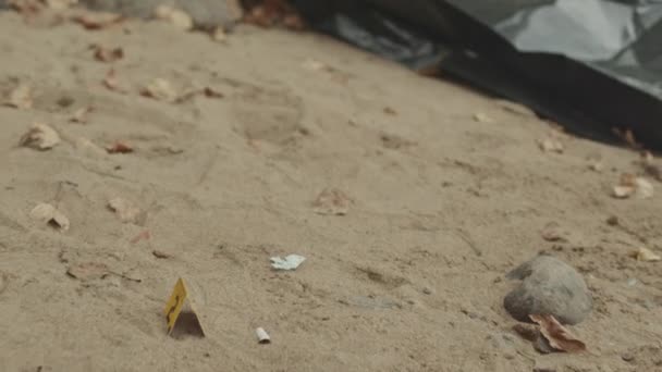 在阴天的早晨 没有人在肮脏的沙滩河岸用黑色塑料袋和黄色标记把无法辨认的尸体放大拍摄出来 — 图库视频影像