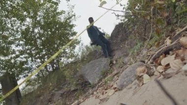 Düşük kesitli fotoğraf, genç Afro-Amerikan adli tıp uzmanı mavi takım elbise giymiş profesyonel dijital kamerayla suç mahallinin fotoğraflarını çekmek için nehir kıyısına iniyor.