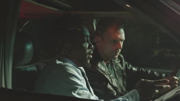 让多族裔的犯罪调查人员在夜间坐在车里看犯罪记录 边聊天边找他 — 图库视频影像