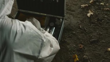 Koruyucu tulumlar üzerine isimsiz bir adli tıp uzmanının plastik poşette yerden kanıt toplayıp gece cinayet mahallinde ilk yardım çantasına koyduğu fotoğraftan.