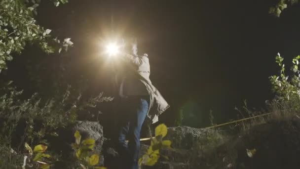 フラッシュライトを使用して武装したアフリカ系アメリカ人男性警察の探偵のミディアムショットは 殺人現場の横の夜の森で容疑者を迫害しながら — ストック動画