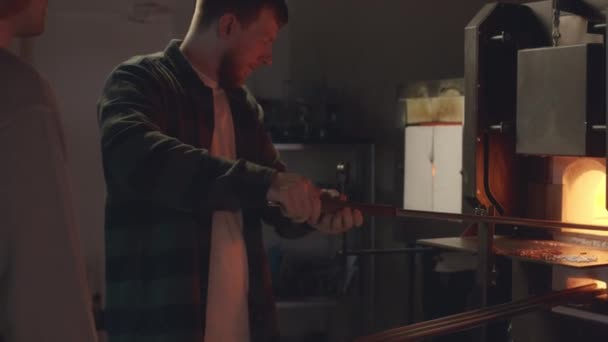 在制造车间里 一名熟练的男性工匠用玻璃杯 教新工人如何在炉边用熔融玻璃工作 — 图库视频影像
