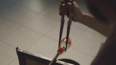 Cımbızla çalışırken atölyedeki üflemeli boruda eriyik cam şeklini alırken omuz üstünden çekilen cam.