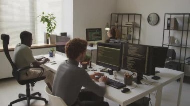 Çağdaş minimalist açık uzay ofisinde birlikte çalışırken, masaüstü bilgisayarlarında üç program kodundan oluşan çok ırklı programcıların arka planı