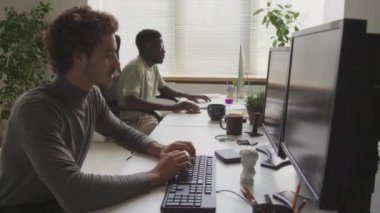 Çağdaş açık uzay ofisindeki masaüstü bilgisayarlarında çalışan iki farklı erkek programcının belini kaldırın