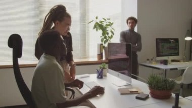 Meslektaşları pencerenin kenarında durup onları izlerken, açık uzay ofisinde birlikte çalışırken bilgisayar monitörüne bakan ve tartışan çeşitli programcıların orta boy görüntüleri.