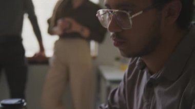 Çift ırklı erkek yazılım mühendisinin ofiste çeşitli meslektaşlarıyla sohbet ederken bilgisayarda klavyeyle veri yazışının eğik görüntüsü