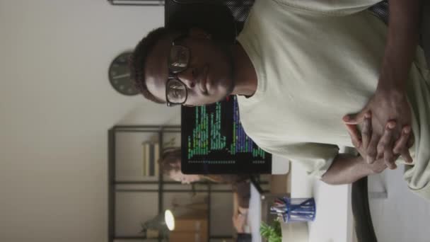 現代のオフィスの職場で椅子に座って座っている若い黒人男性プログラマーの垂直中型の肖像画 — ストック動画