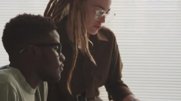 拥有长发的年轻白人女性和在办公室里看着电脑台式电脑和聊天的非裔美国年轻人 — 图库视频影像