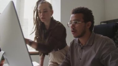 Bilgisayar monitörüne bakıp işaret eden ve bilgiyi analiz ederken tartışan iki çok ırklı meslektaşın orta boy fotoğrafı.