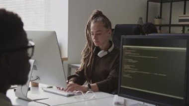 Açık uzay ofisindeki çeşitli iş arkadaşlarıyla birlikte çalışırken, kablosuz klavyede rasta program kodunu yazan Kafkasyalı genç bir kadın programcının belden yukarı görüntüsü.