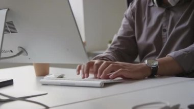 Ofiste çalışırken gözleri bilgisayar ekranında hareket ettiren ve kablosuz klavyede program kodunu yazan odaklanmış genç adamın eğik görüntüsü