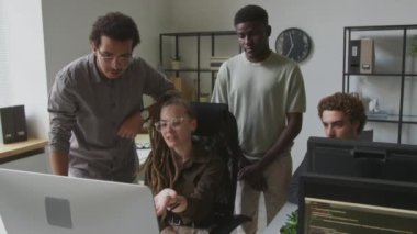 Kafkasyalı genç bir kadın programcının açık uzay ofisinde birlikte çalışırken çeşitli erkek meslektaşlarıyla bilgisayardaki yazılımı tartışırken orta boy görüntüsü.