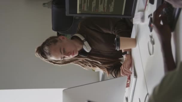 黒人男性の同僚とオフィスのデスクトップコンピュータで作業中にワイヤレスキーボードにタイピングするドレッドロックを持つ若い白人女性ソフトウェアエンジニアの垂直ウエストアップショット — ストック動画