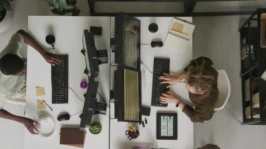 Modern açık uzay ofisindeki beyaz ofis masasında yan yana otururken masaüstü bilgisayarlarında kodlama yapan çok ırklı programcıların üst görünümü