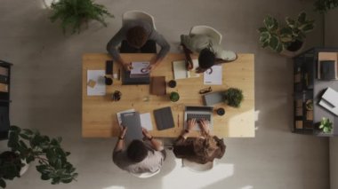 Modern ofisteki ahşap masada toplanırken, dört kişilik çok ırklı iş ekibinin en iyi görüntüsü mali raporu analiz ediyor.