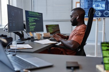 Yüksek teknoloji ofisindeki bilgisayarlarla çalışan siyah yazılım mühendisinin yan görünüm portresi, boşluğu kopyala
