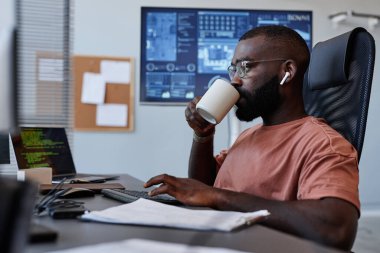 IT yazılım geliştirme bölümünde çalışırken işyerinde kahve içen siyahi adamın yan görünüm portresi