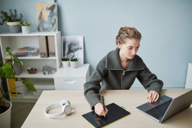 Genç tasarımcı ofisindeki grafik tabletinde online proje üzerinde çalışıyor.