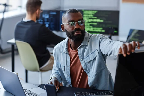 Portrait of black man adjusting computer screens while writing software code in office