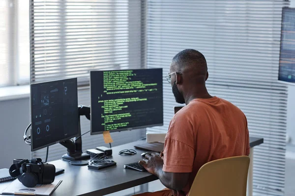 Minimal back view of African American man writing code in green lines and using computers in office, copy space