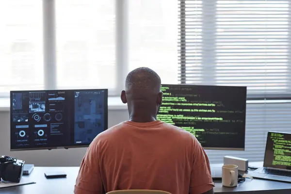 Back view of African American man using computers with data and code lines in office, copy space