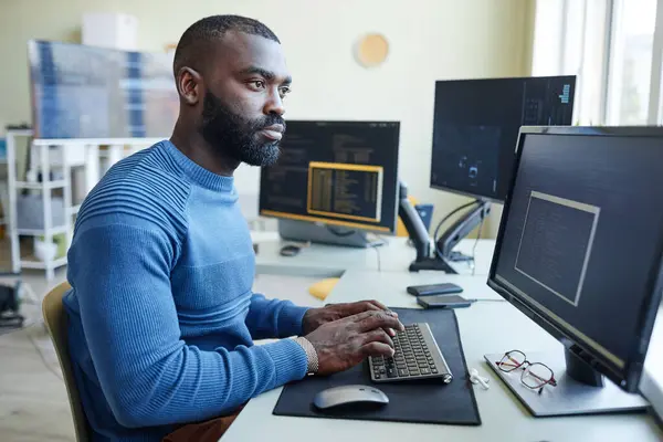 Side view portrait of African American man as computer programmer writing code at office workplace