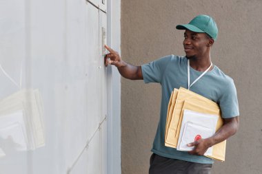 Gülümseyen teslimatçının kapı zilini çalıp paketleri tutarken yan görünüm portresi