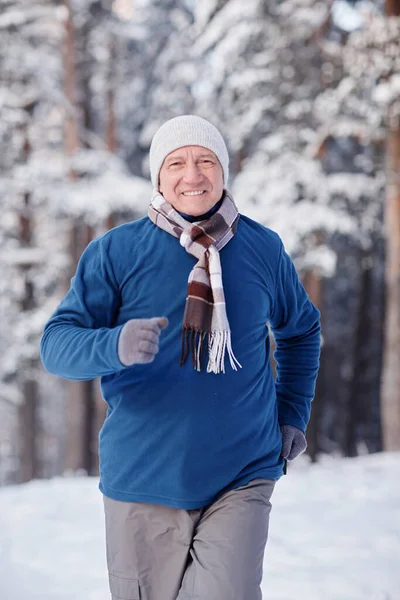 Vertical portrait of sportive senior man in winter forest running towards camera with smile