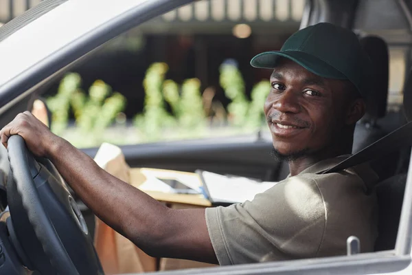 Portrait of young black man driving delivery truck and smiling at camera out window